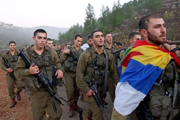 A newly-recruited Israeli paratrooper draped in the Druze flag marches with others in full combat gear on a 50-kilometer 12-hour hike in the mountains near Jerusalem on November 10, 2022.