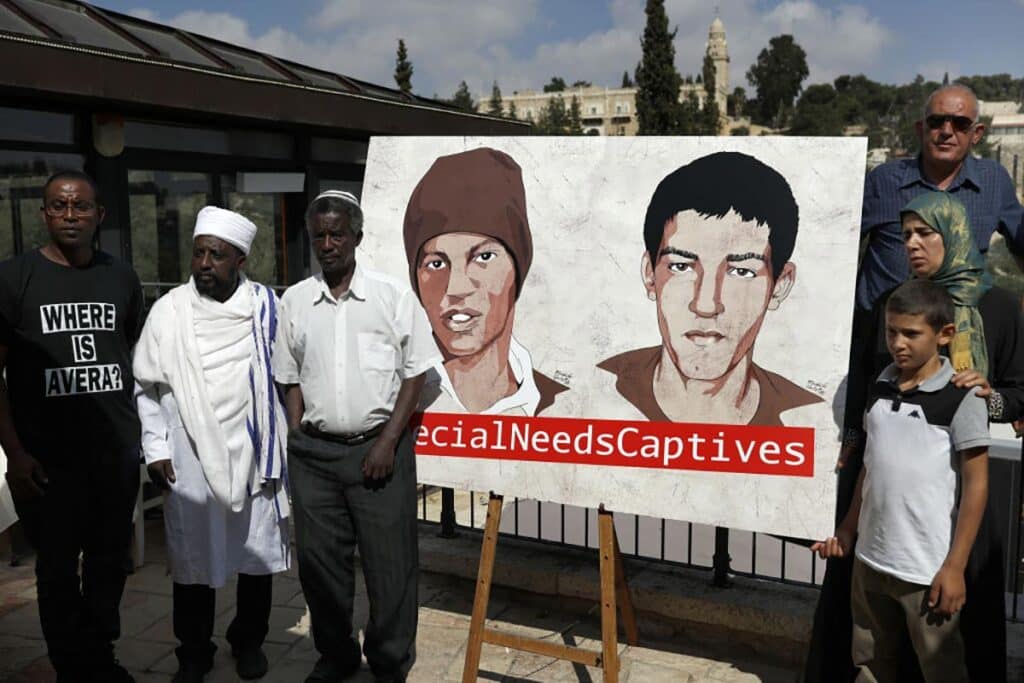 Relatives of Hisham Al-Sayed (C-R) and Avera Mengistu (C-L), two Israelis held by Hamas in Gaza since 2014, pose for a picture next to a painted poster depicting them after a press conference organised by the captives' families calling for their release, in Jerusalem on September 6, 2018. Al-Sayed and Mengistu, two Israeli citizens who are mentally ill, are being held captive by Hamas after having crossed into the Gaza Strip.