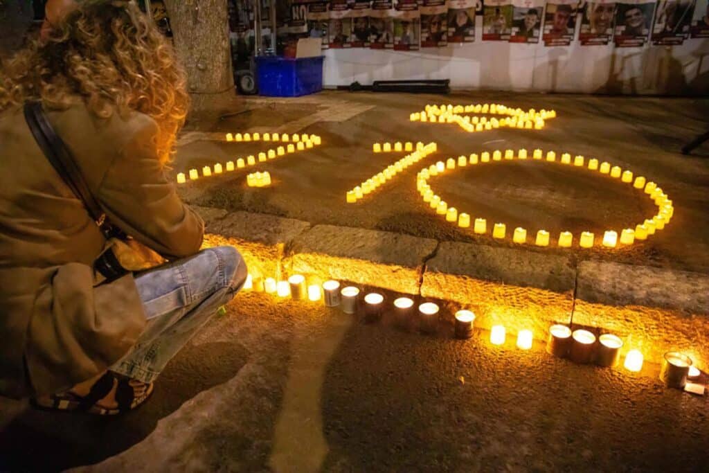 A demonstrator lights a candle next to candles in the shape of the 10/7, At the memorial service marking a month since the October 7 massacre at the Knesset of Israel.